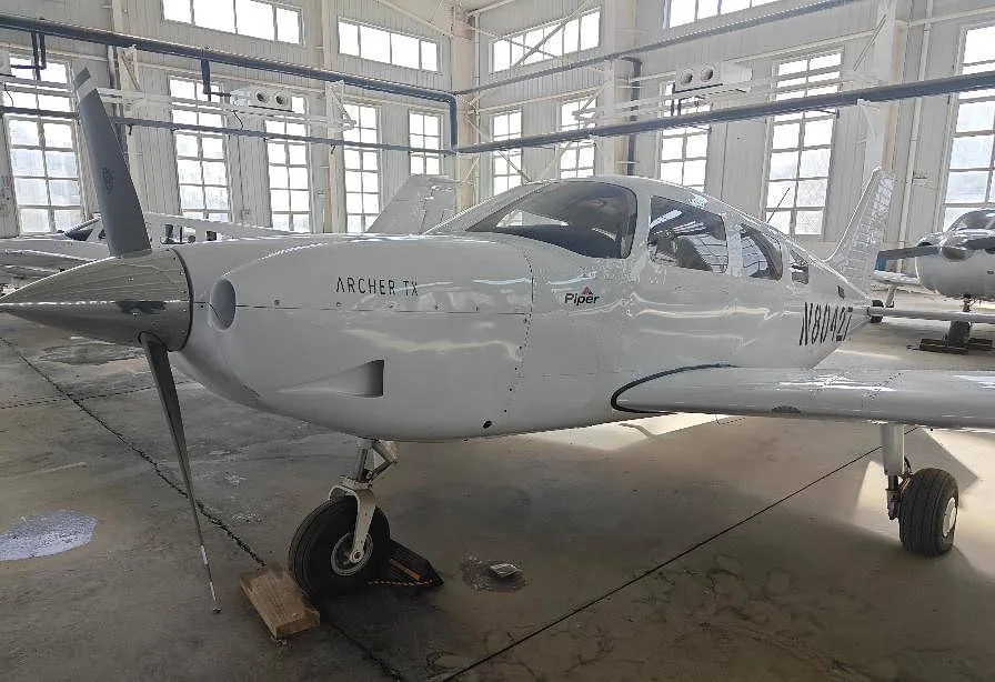 A white Piper Archer TX aircraft with registration N80427 is parked in a hangar, viewed from the front-left.