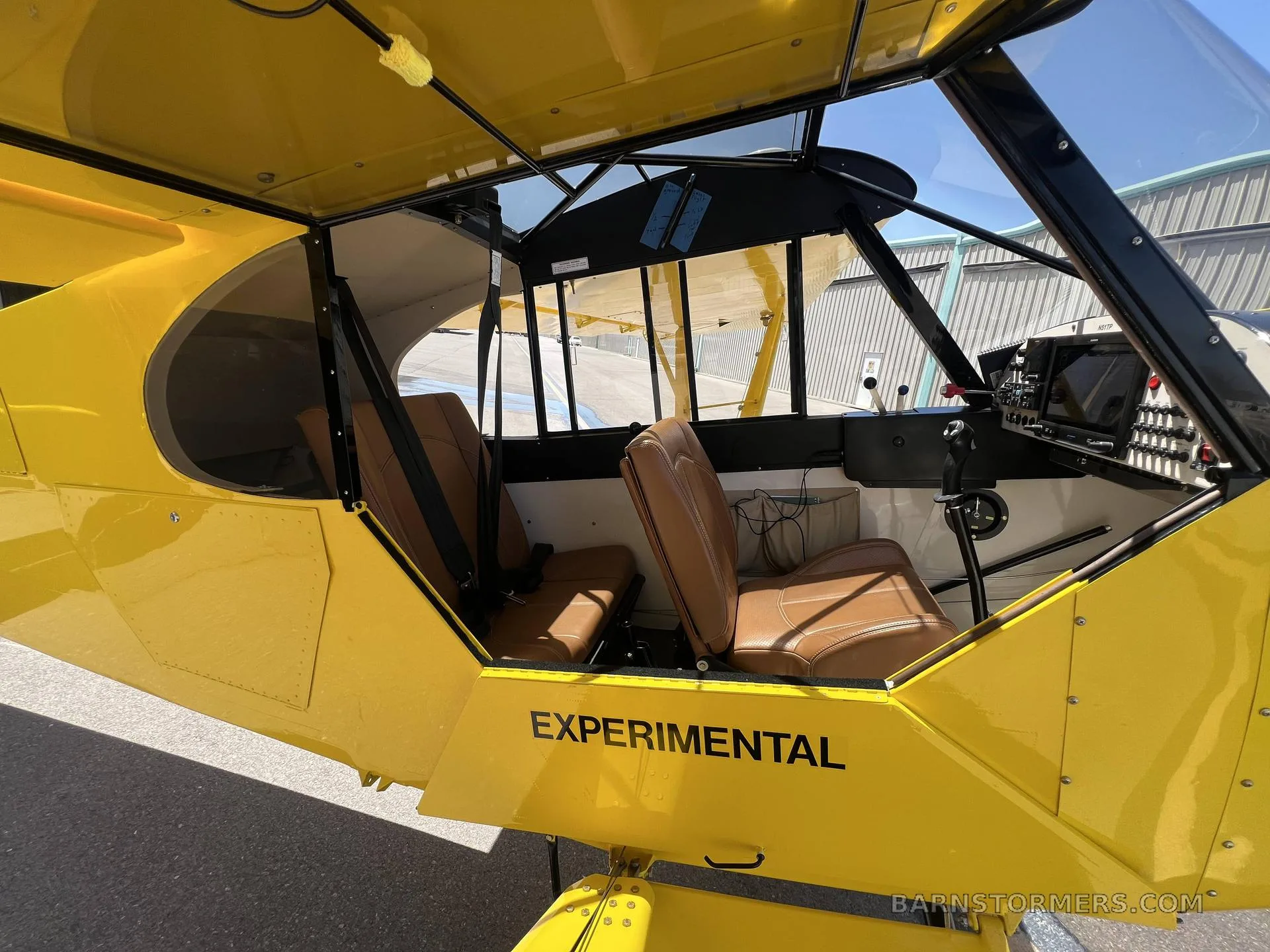 The interior cabin of a yellow experimental aircraft, showing two brown leather seats and part of the instrument panel.