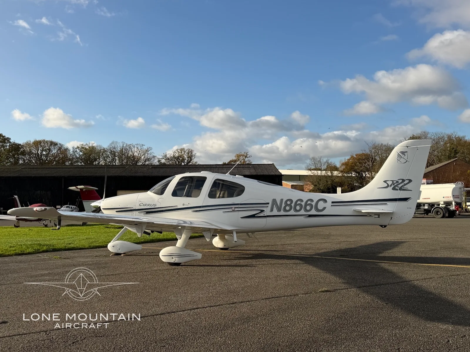 A side view of a white Cirrus SR22 aircraft with black and grey stripes, registration N866C, parked on an asphalt apron.