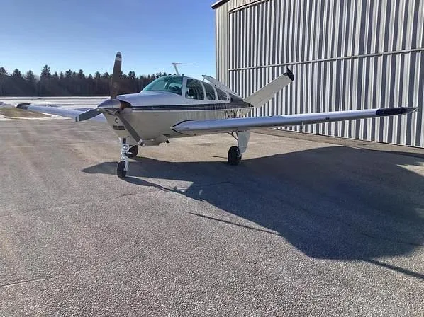 A beige and blue single-engine aircraft with registration C-GXOZ is parked nose-first next to a metal hangar.