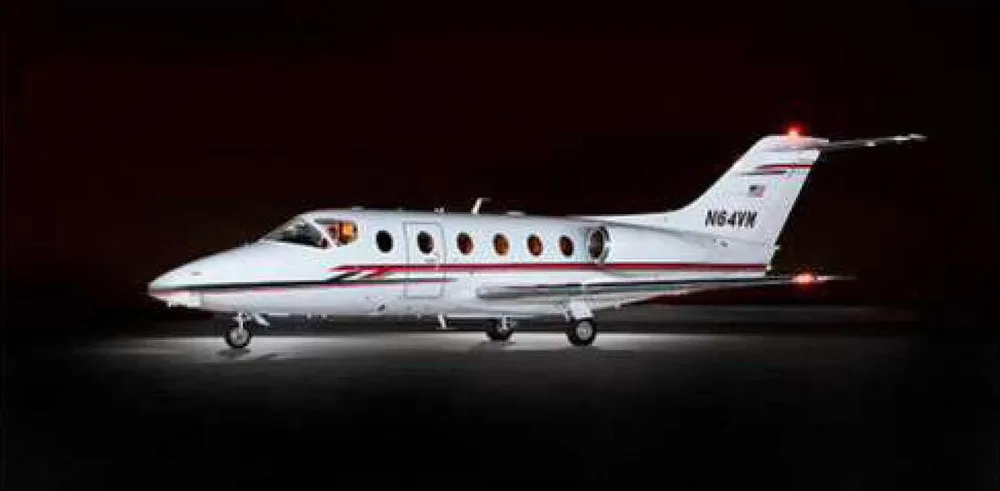 A white business jet, likely a Hawker, with red and black stripes, illuminated at night, showing the registration N64VM on the tail.