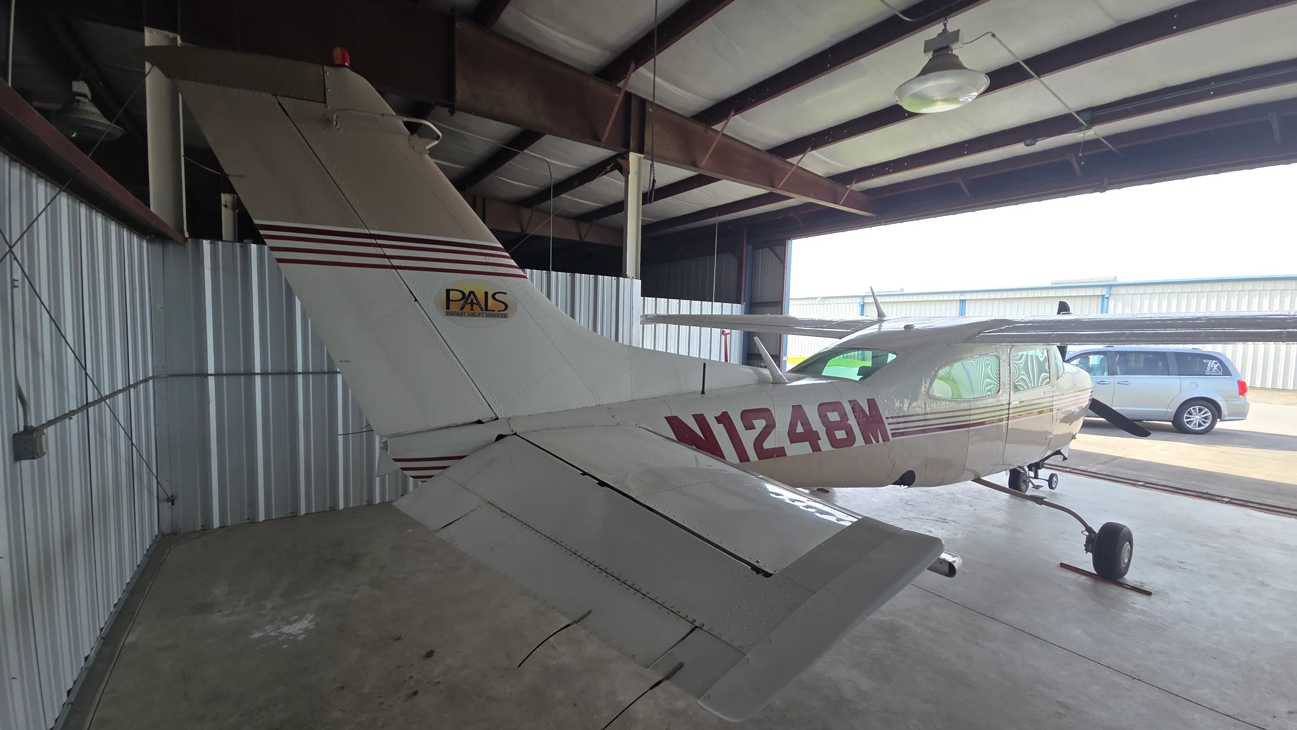 A rear-side view of a white and tan single-engine propeller aircraft with red stripes and registration N1248M, parked in a hangar.