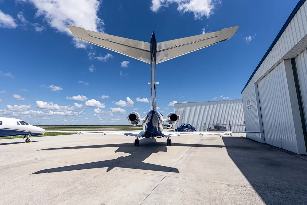 A rear view of the white and blue Cessna Citation III business jet, N650AT, parked on an airfield next to a hangar.