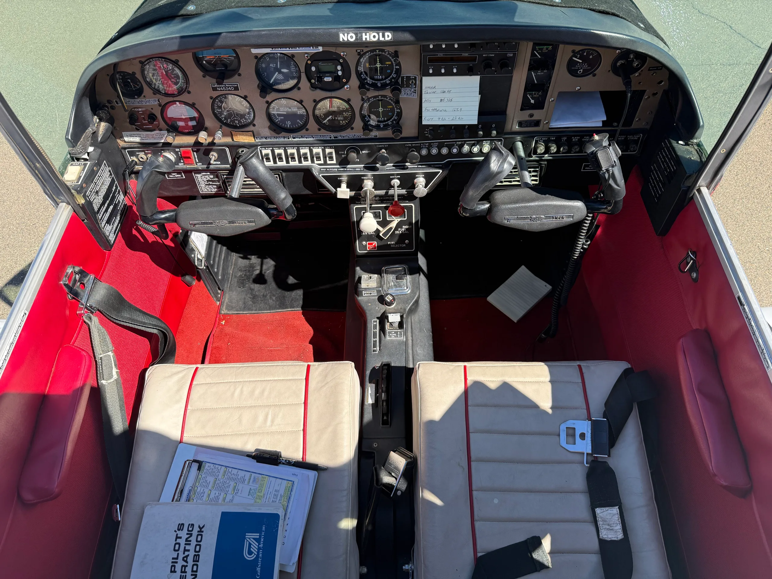 An overhead view of the aircraft's cockpit and front seats, showing the instrument panel and red carpet.