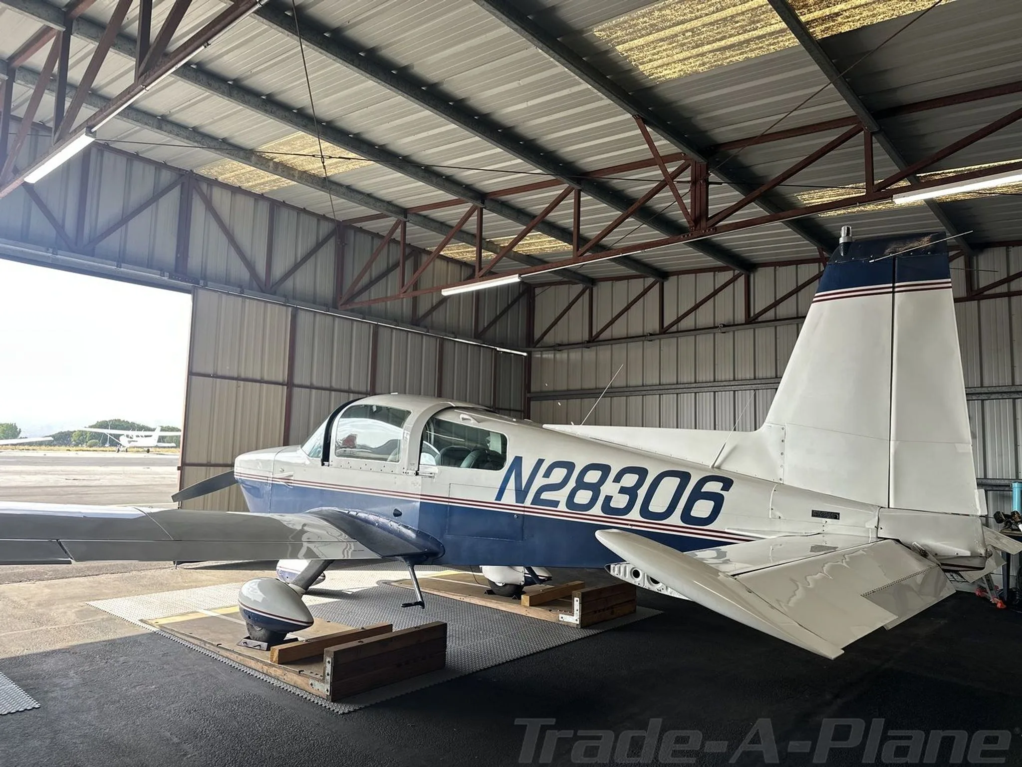 A blue and white Grumman AA5B Tiger aircraft, N28306, parked in a hangar, viewed from the rear right.