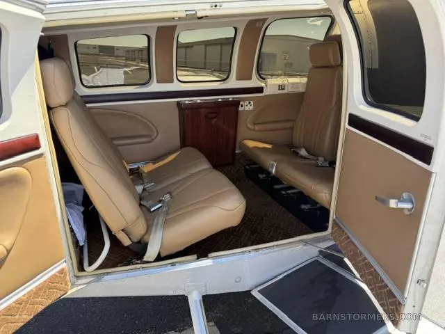 The tan leather interior cabin of a small aircraft, showing two rows of seats and a small cabinet.