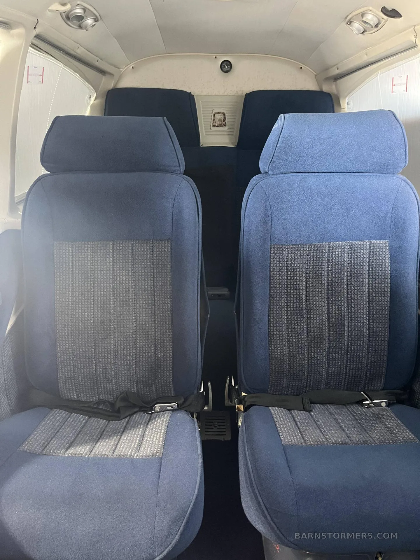 Two rows of blue fabric aircraft seats with seatbelts in the cabin interior.