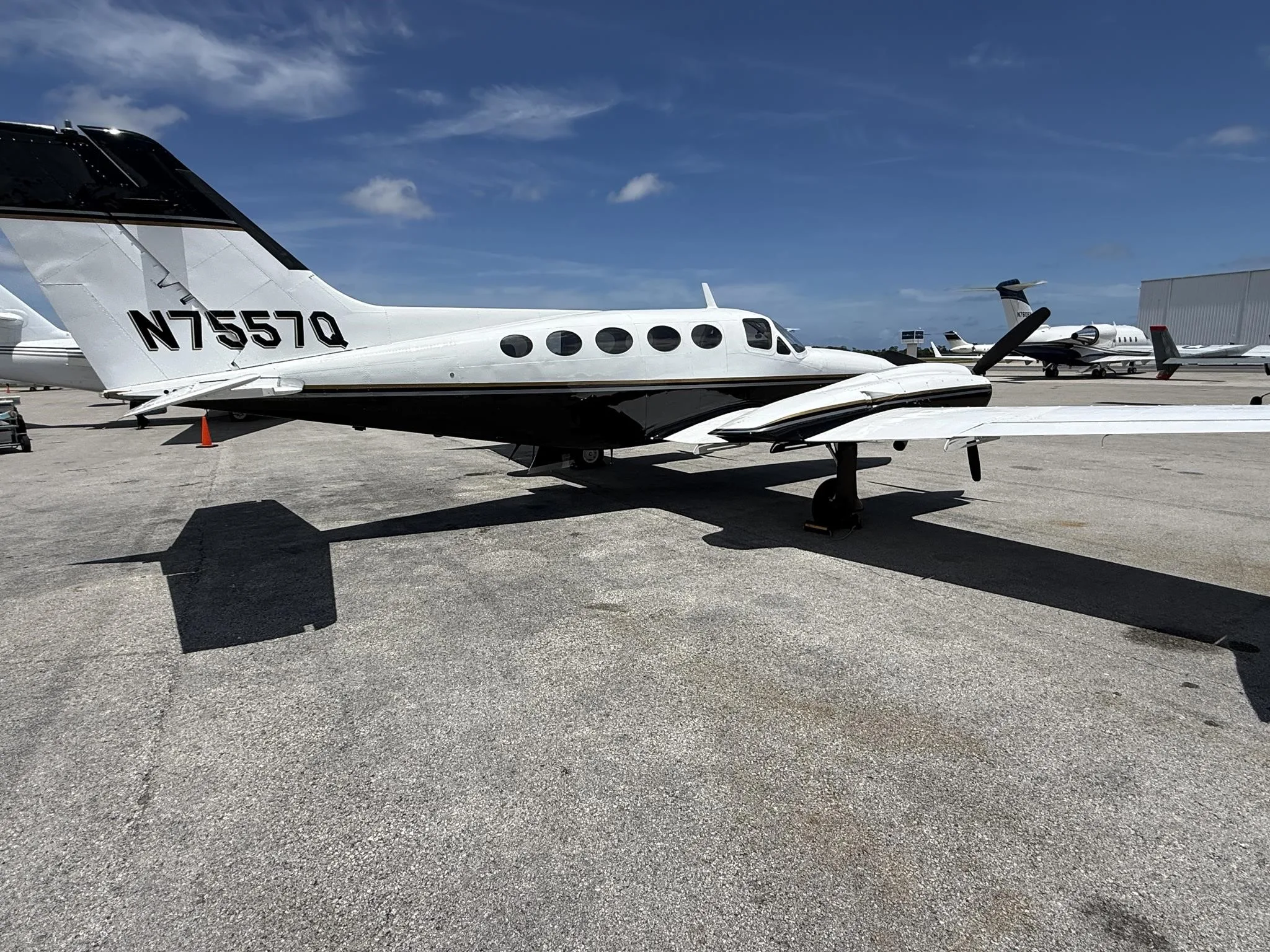 A rear-side view of the white and black twin-engine propeller aircraft N7557Q, showing the tail number.