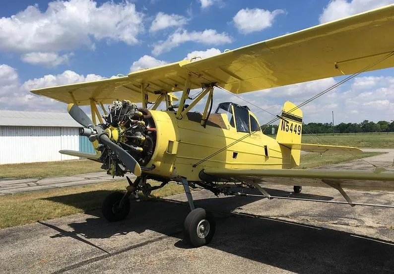 A yellow biplane crop duster, N5449, seen from the front-right on an airfield.