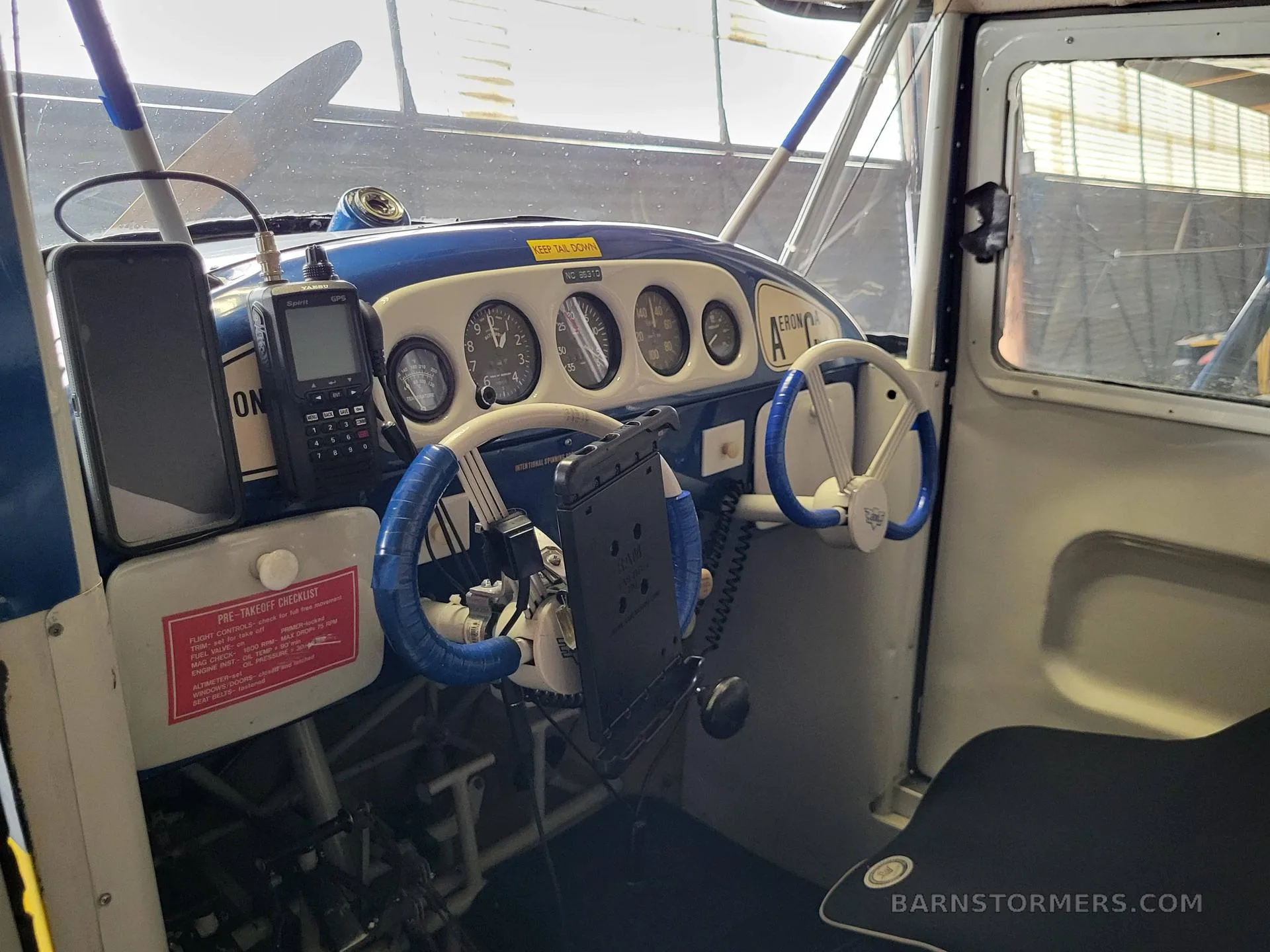 The cockpit of an Aeronca Champ shows a blue and white instrument panel with dual yokes and a mounted GPS unit.
