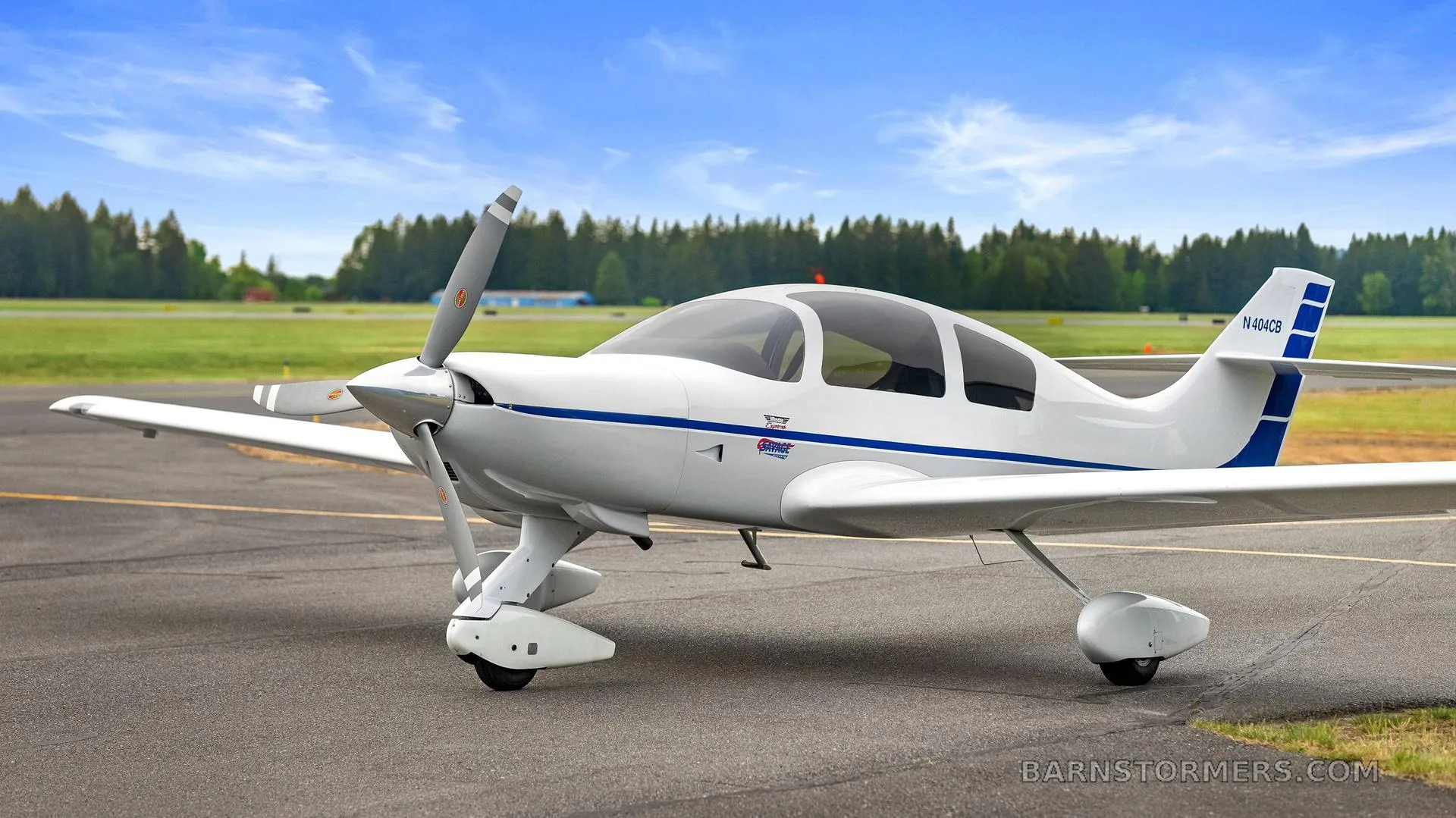 A white single-engine aircraft with blue stripes, registration N404CB, parked on an asphalt runway with trees in the background.