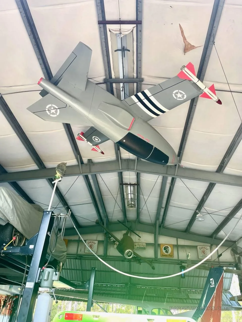 A grey model aircraft with black and white stripes and red wingtips, hanging from the ceiling of a hangar.
