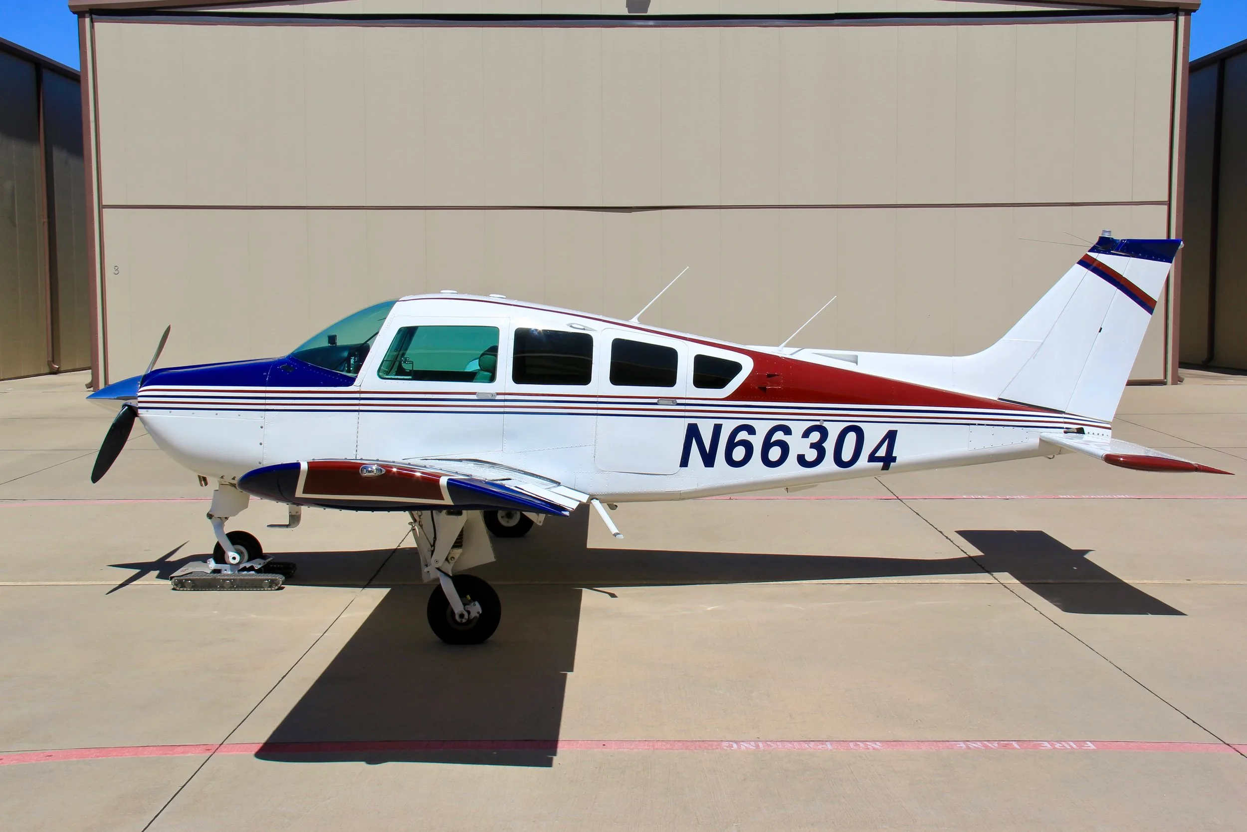 A side profile of the white, blue, and red single-engine aircraft (N66304) parked on an tarmac.