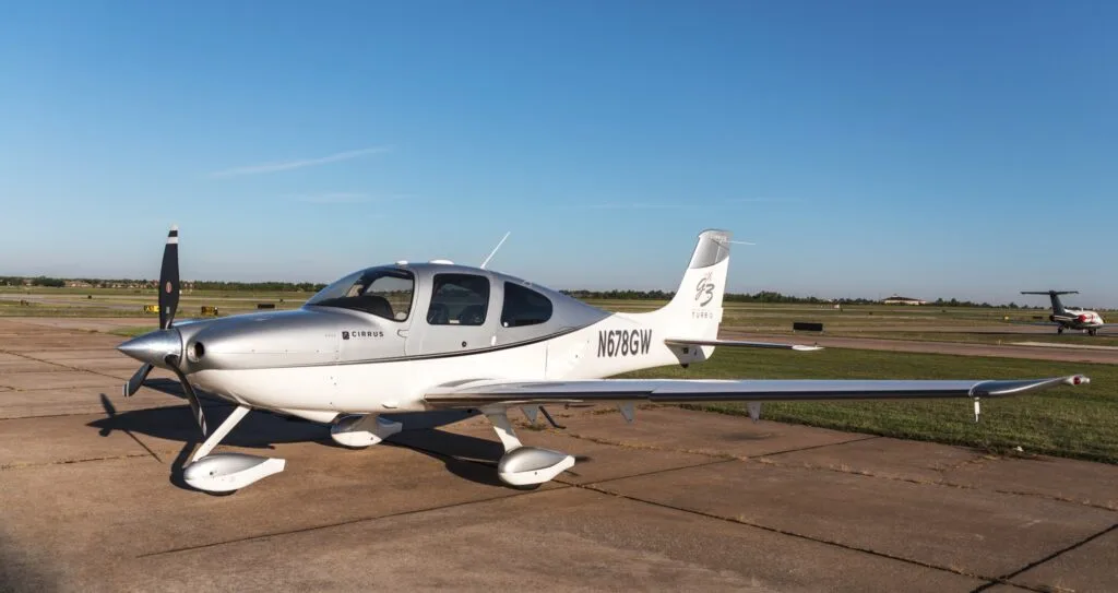 A silver and white Cirrus SR22 G3 Turbo aircraft (N678GW) parked on an airfield under a clear blue sky.