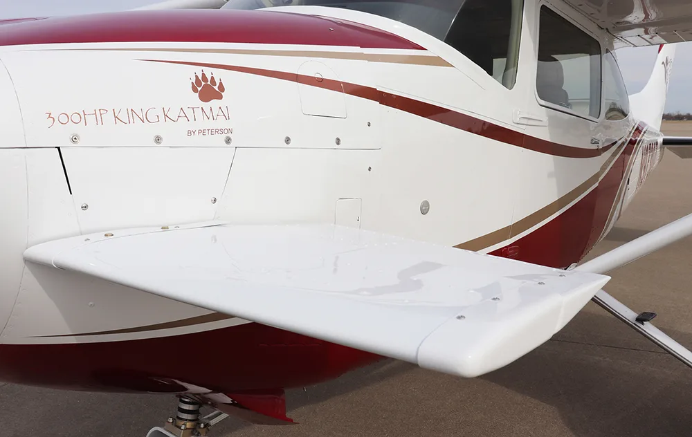 A close-up of the fuselage of a white and red aircraft, showing '300HP KING KATMAI' text and a paw print logo.