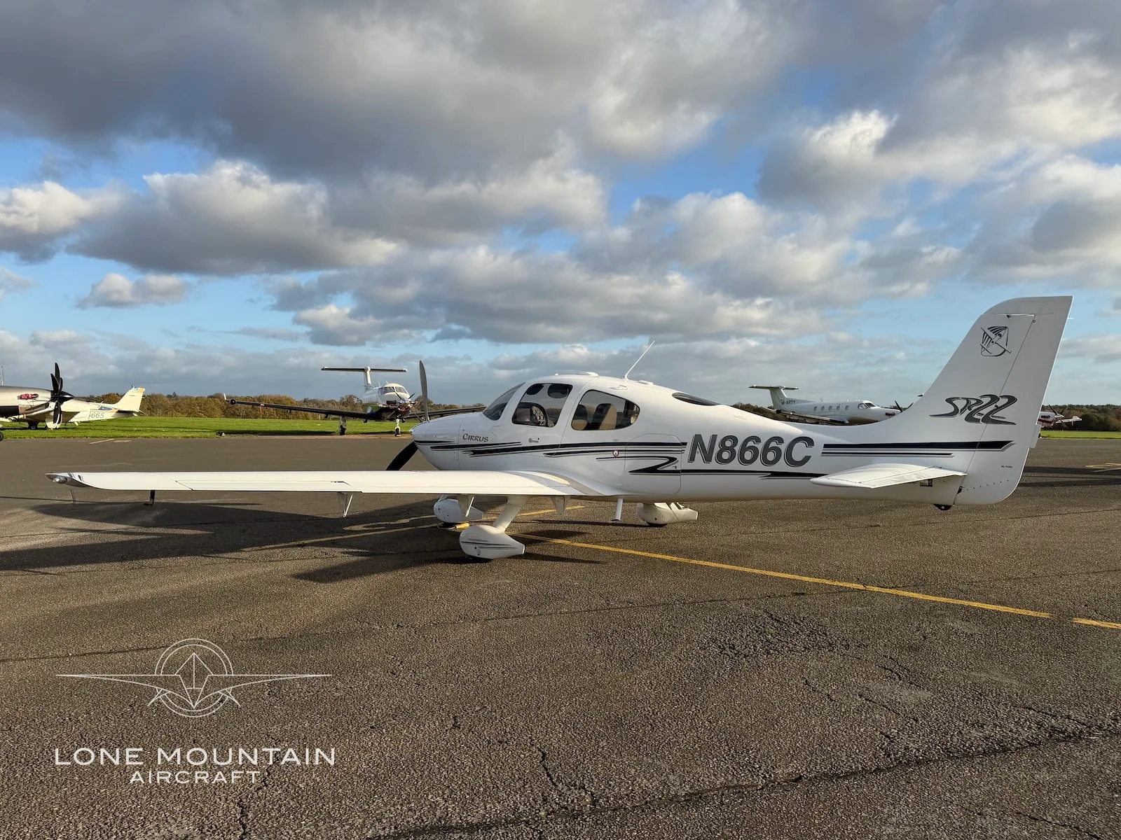 A three-quarter rear view of a white Cirrus SR22 aircraft with black and grey stripes, registration N866C, parked on an asphalt apron.