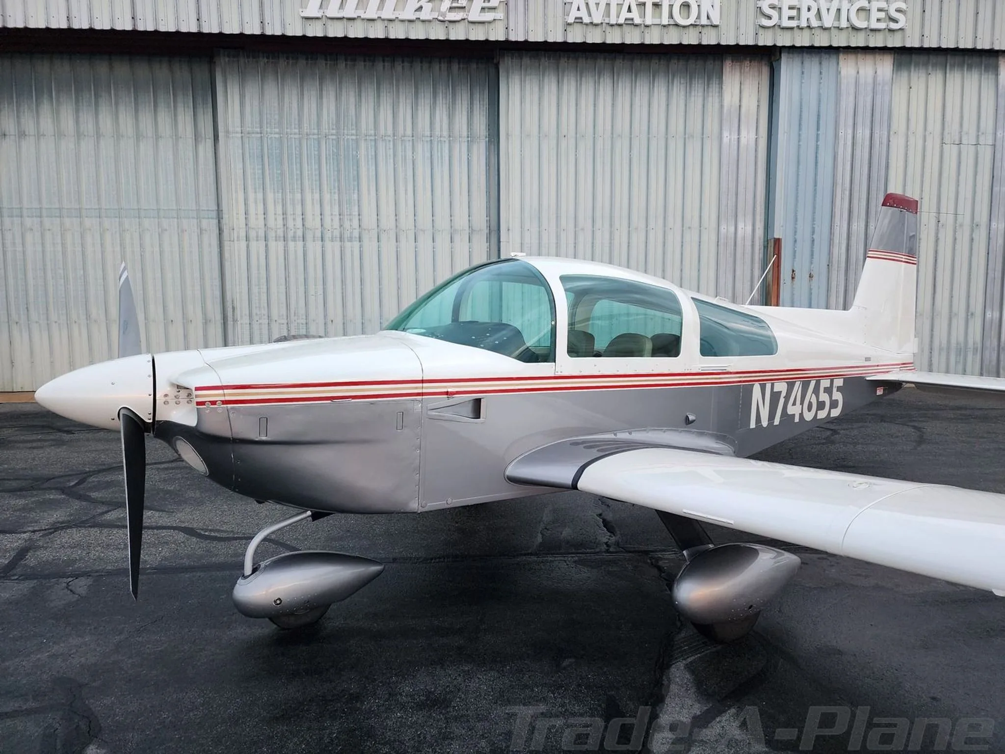 A close-up side view of the white and grey Grumman American aircraft, N74655, showing its propeller and landing gear.