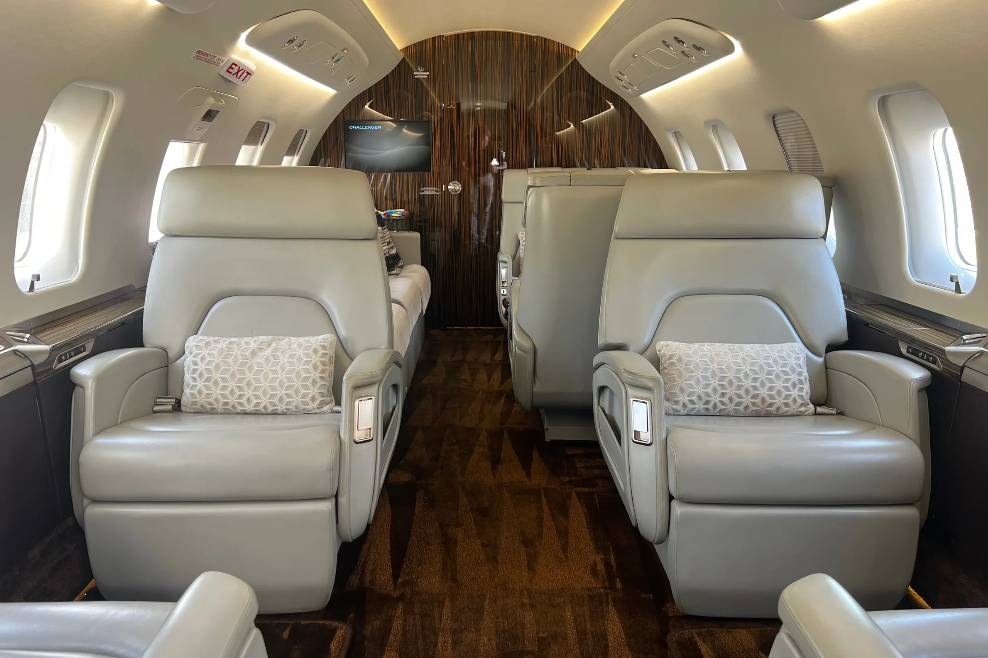 Aisle view of an aircraft cabin with light grey leather seats.