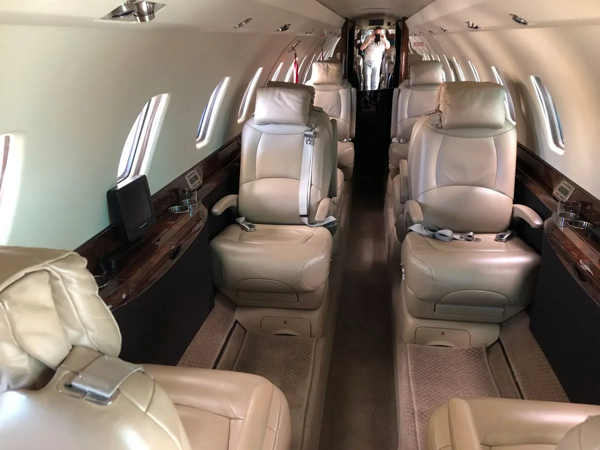 The interior cabin of a private jet with beige leather seats and a person in the background.