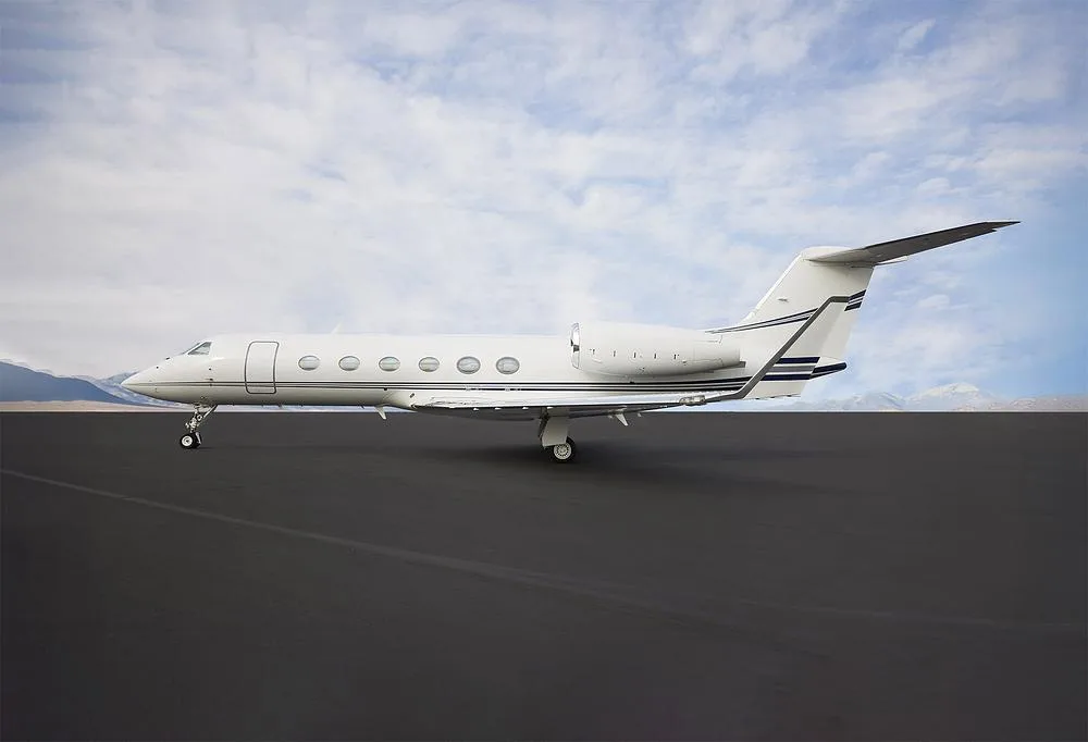 Side view of a white Gulfstream G550 business jet with dark blue stripes on a tarmac.