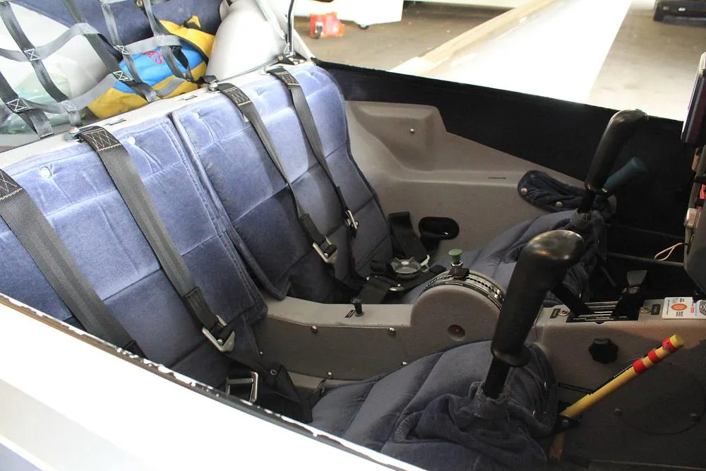 The blue fabric seats and interior cabin of a light aircraft, showing control sticks and harnesses.