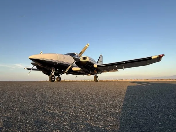 A low-angle view of a silver and black single-engine aircraft parked on an asphalt runway under a clear sky.