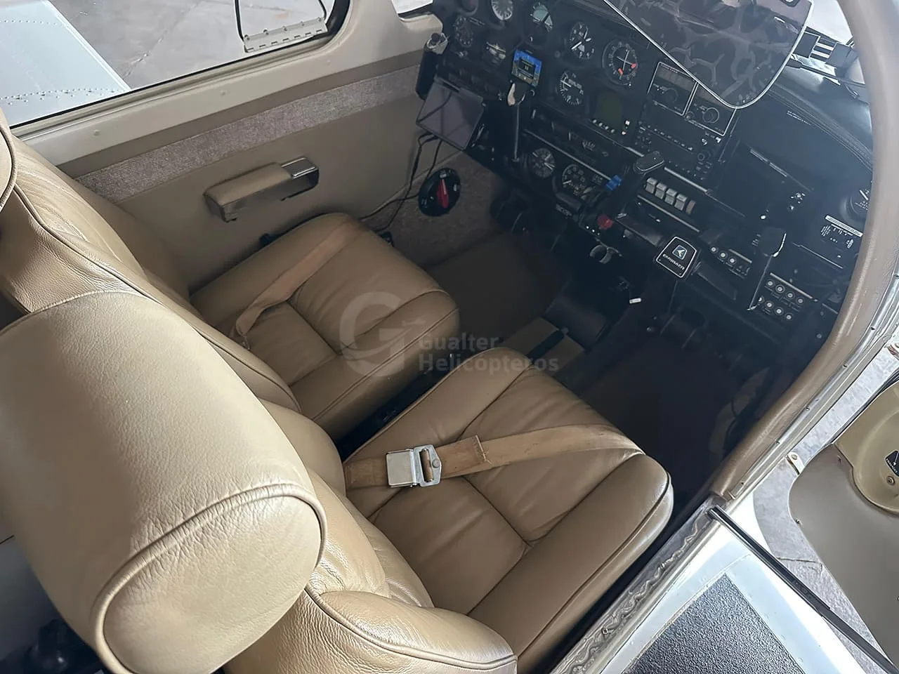 The tan leather pilot and co-pilot seats of a small aircraft, with the instrument panel visible in the background.