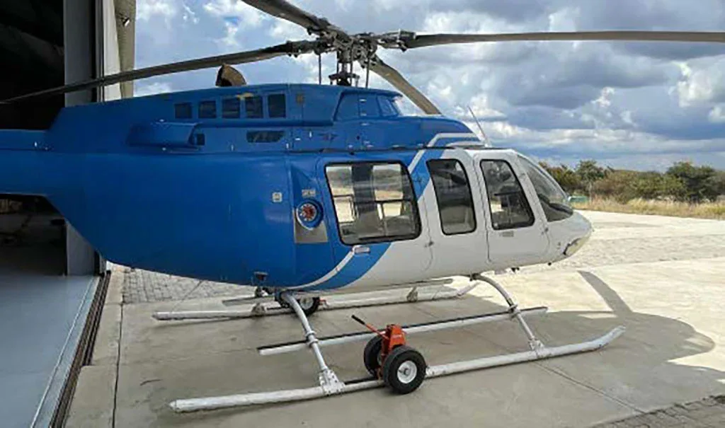 A blue and white helicopter, viewed from the side, parked on concrete outside a hangar.