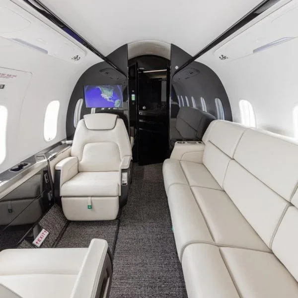 An interior view of a private jet cabin featuring a cream leather sofa and individual seats.