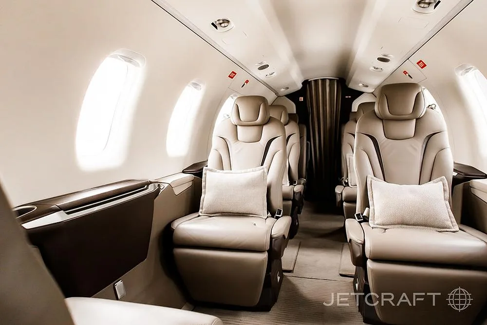 A close-up view of the tan leather seats in an aircraft cabin, with windows on the left.