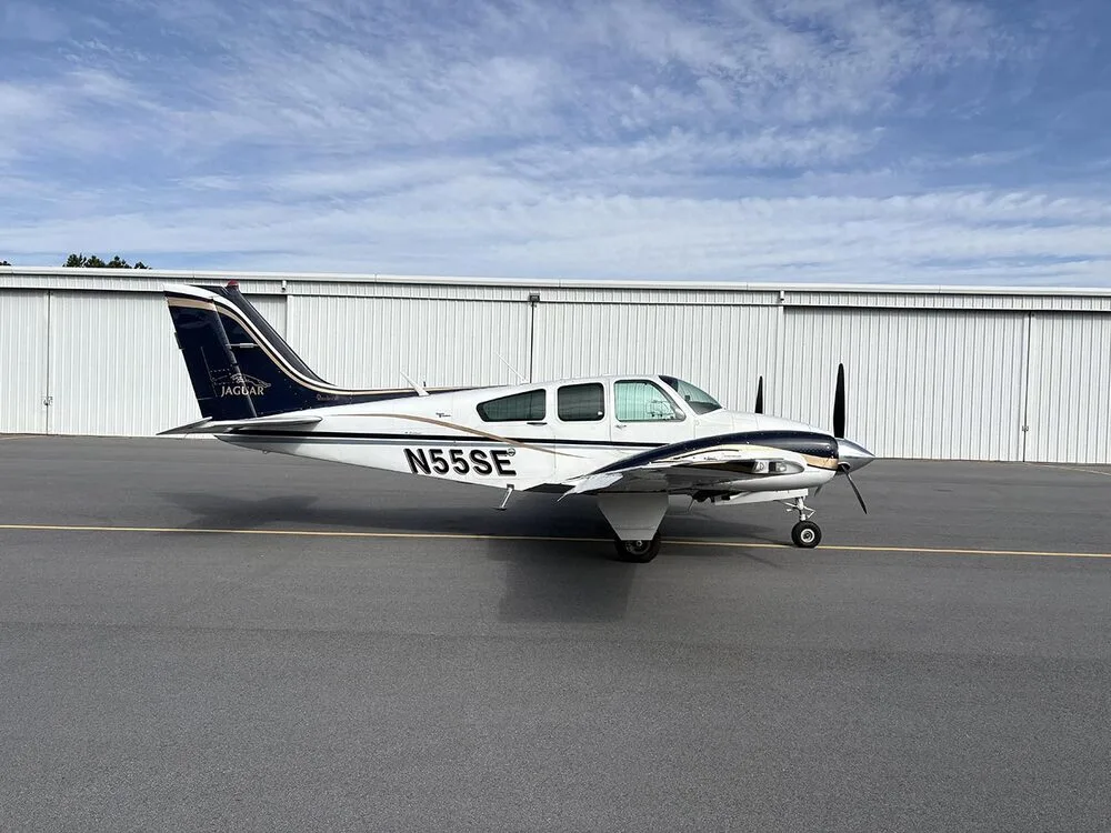 A white and dark blue twin-engine aircraft with registration N55SE is parked on the tarmac, viewed from the right side.