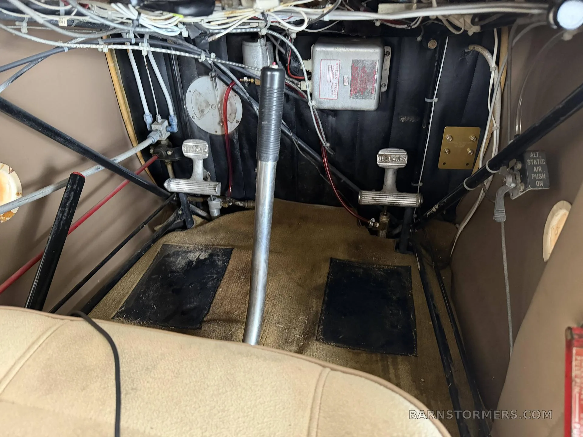 The interior of an aircraft cockpit, showing the rudder pedals, control stick, and various cables and levers.