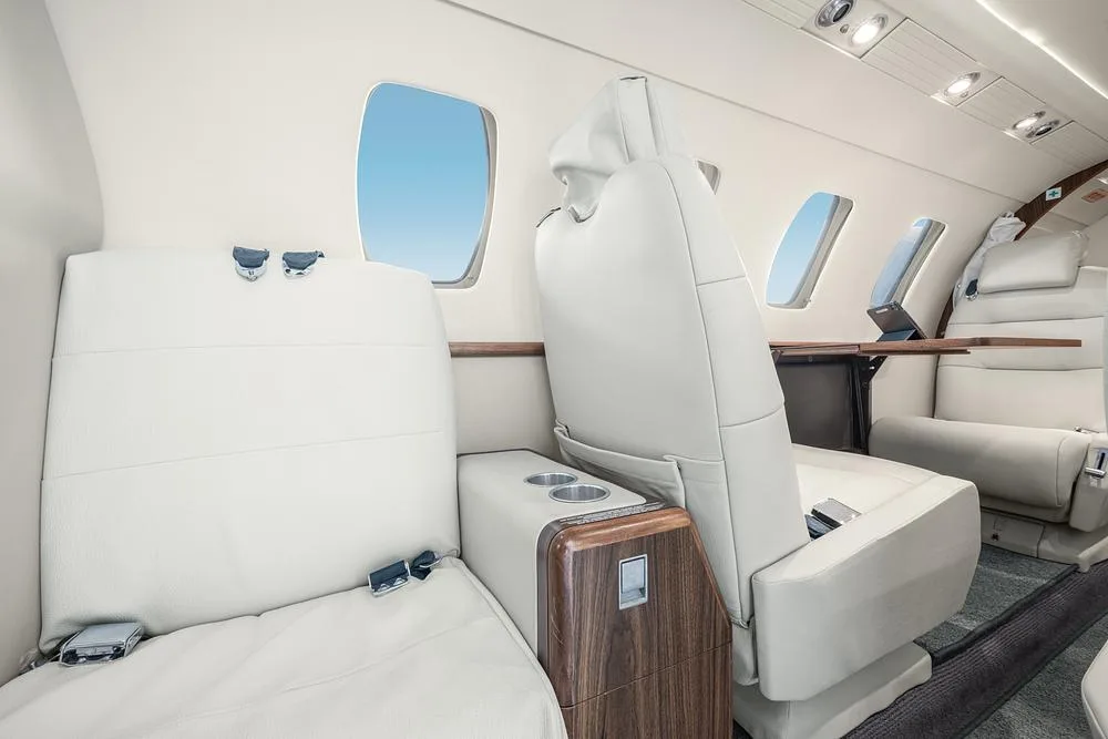 A close-up view of the light leather seats and wooden accents in the private jet's cabin.