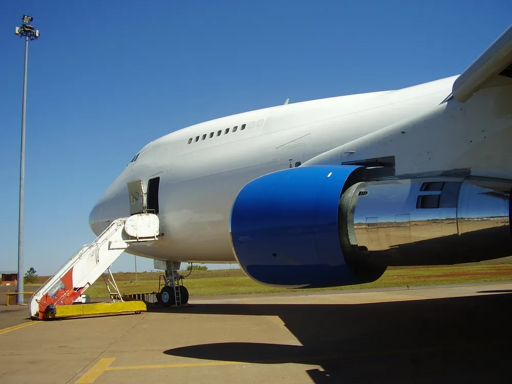 A close-up view of the front fuselage and blue engine of a white Boeing 747, with a passenger stair attached.