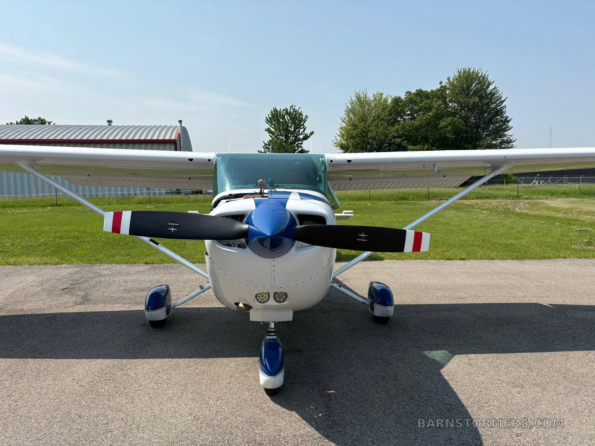 A head-on view of a white and blue single-engine propeller aircraft, likely a Cessna 172, parked on an asphalt ramp.