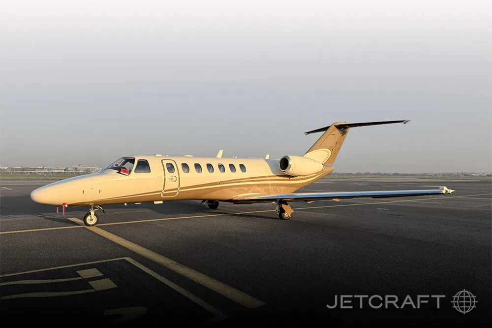 A beige and brown Cessna Citation business jet parked on an airport tarmac under a clear sky.