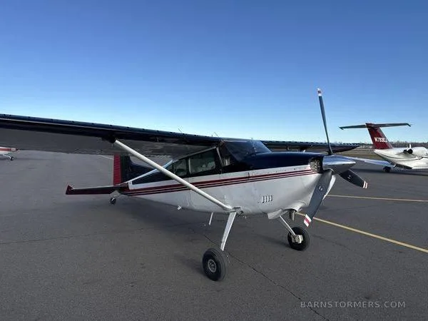 A three-quarter front view of a white and black single-engine propeller aircraft with red accents, parked on an asphalt tarmac.