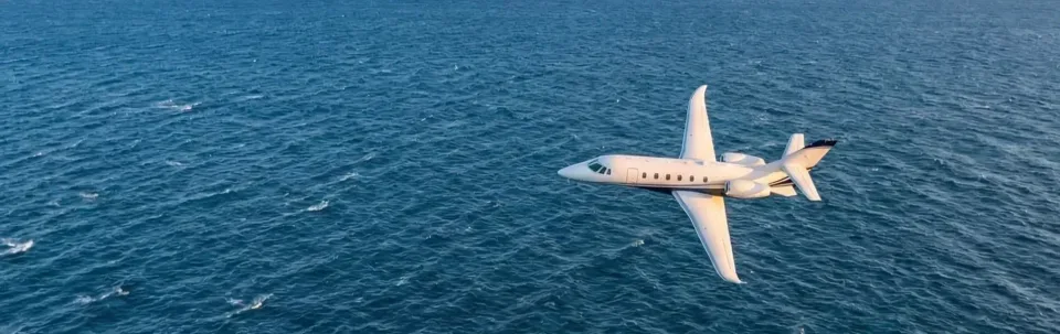 A white private jet flies over the ocean.