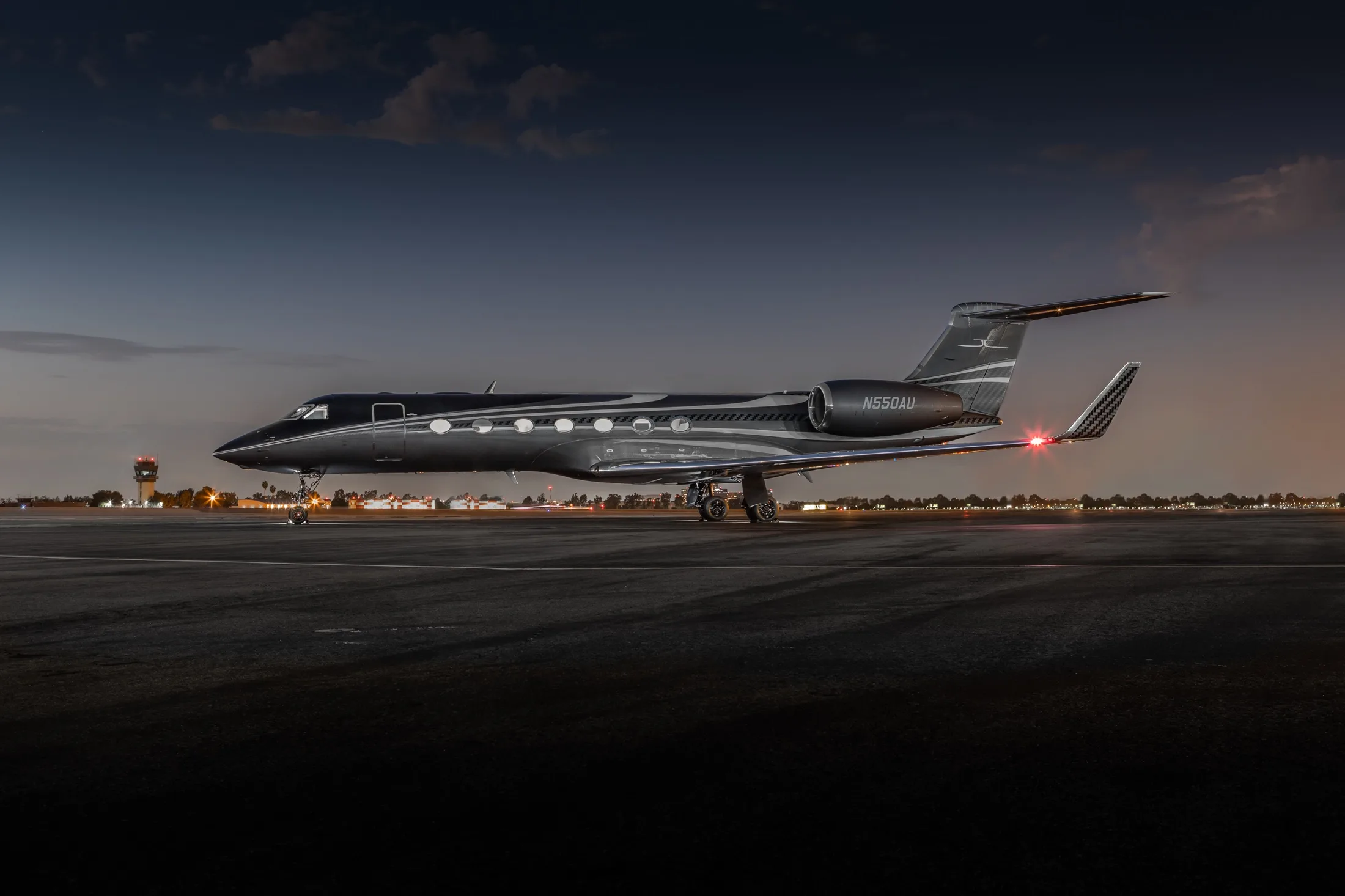A dark grey Gulfstream G550 business jet with registration N550AU parked on an airfield at dusk.