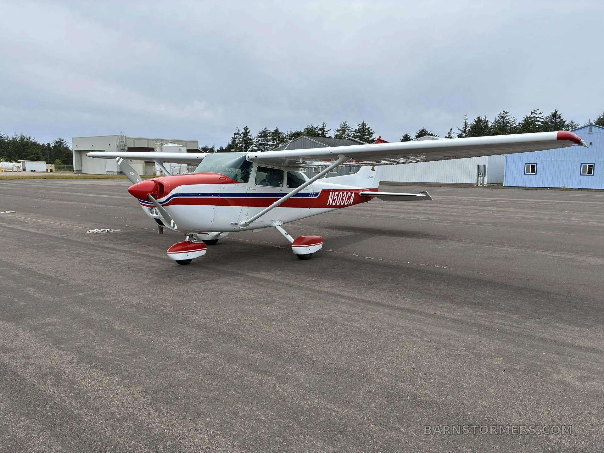 A white and red Cessna 172 Skyhawk II (N503CA) parked on an asphalt ramp with buildings and trees in the background.