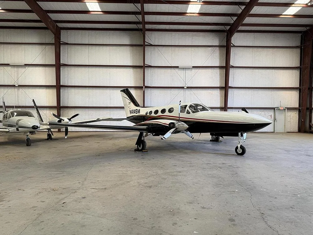 A white and black twin-engine aircraft, N414SM, with gold trim, parked inside a hangar, viewed from the right side.