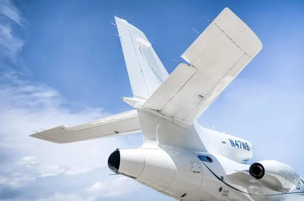 A close-up view of the T-tail and rear-mounted engines of a white Dassault Falcon 900EX business jet, registration N47NS.