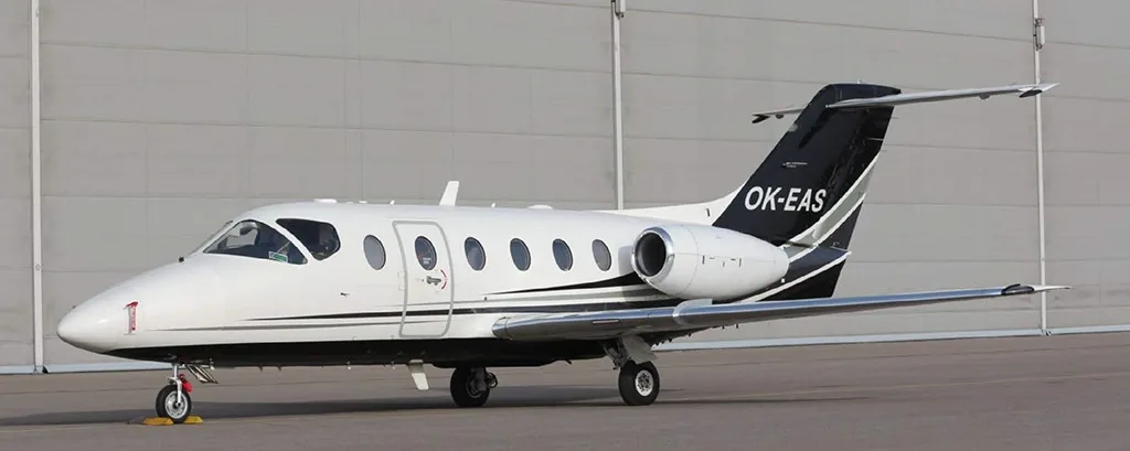 A white and black business jet, likely a Hawker 400XP, with registration OK-EAS, parked on an airfield next to a hangar.