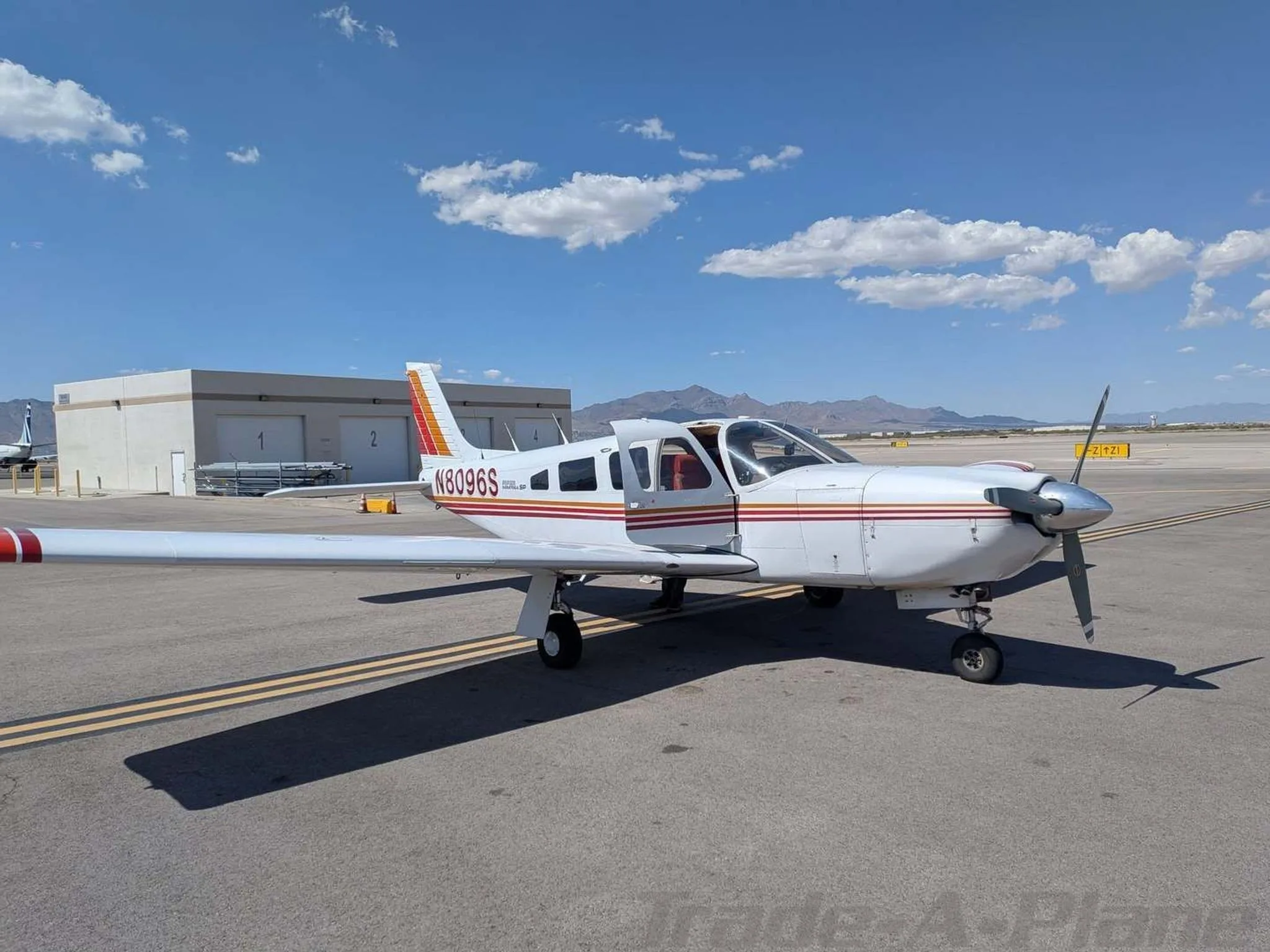 A white Piper PA-28-181 Archer II with red and orange stripes parked on an airfield.