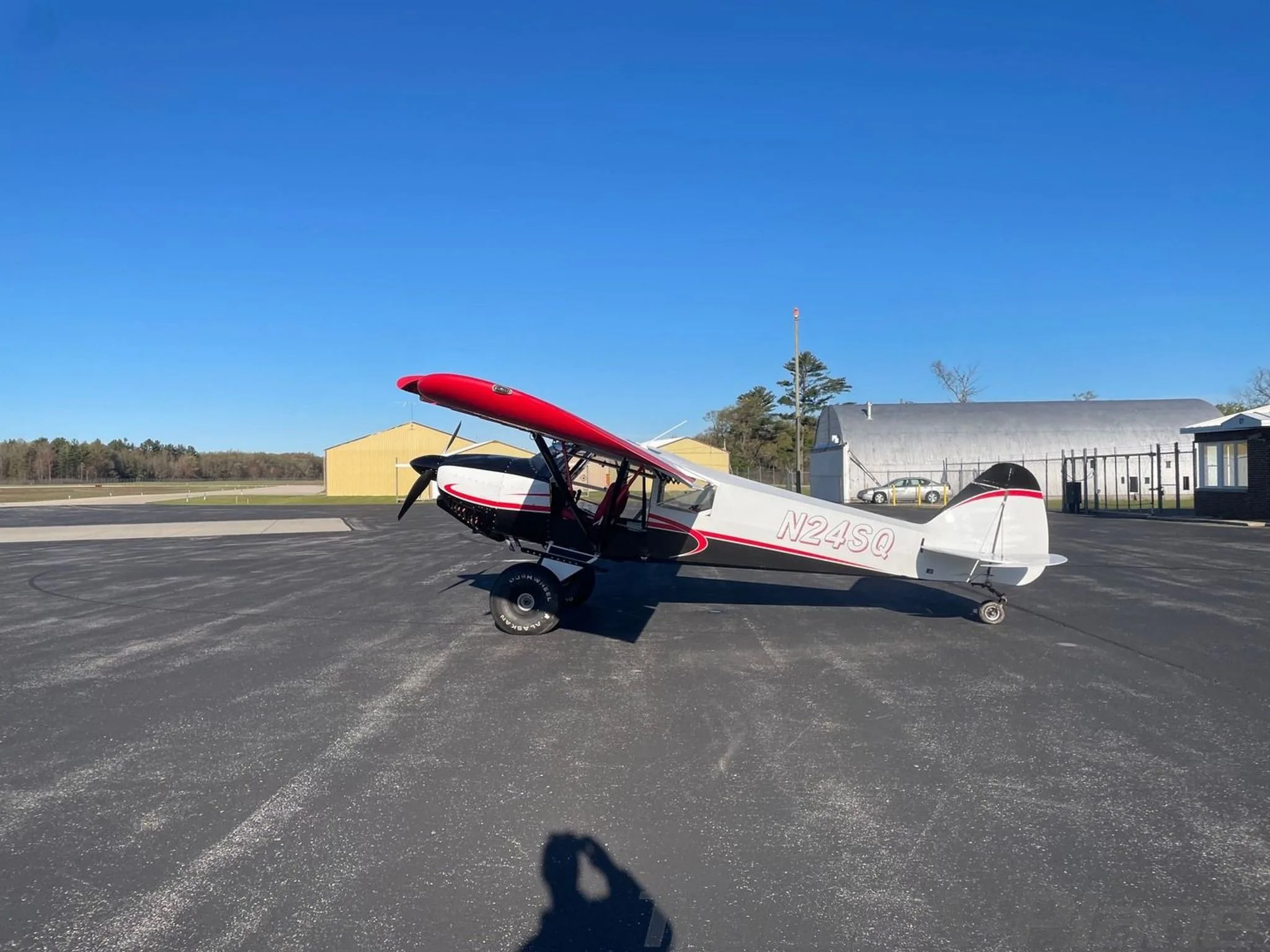 A white, black, and red STOL Quest 4 aircraft (N24SQ) is parked on an asphalt tarmac under a clear blue sky.