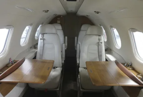 The interior of the aircraft features white leather seats and wooden tables.