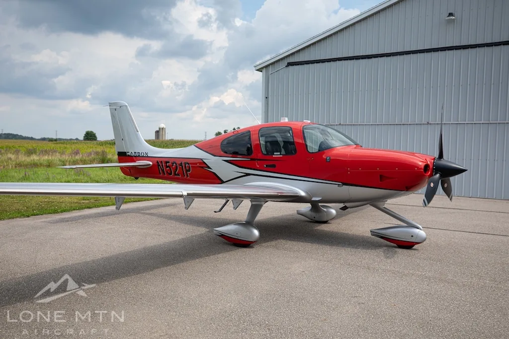 A red and silver Cirrus SR22 aircraft, N521P, parked on an asphalt ramp in front of a hangar.