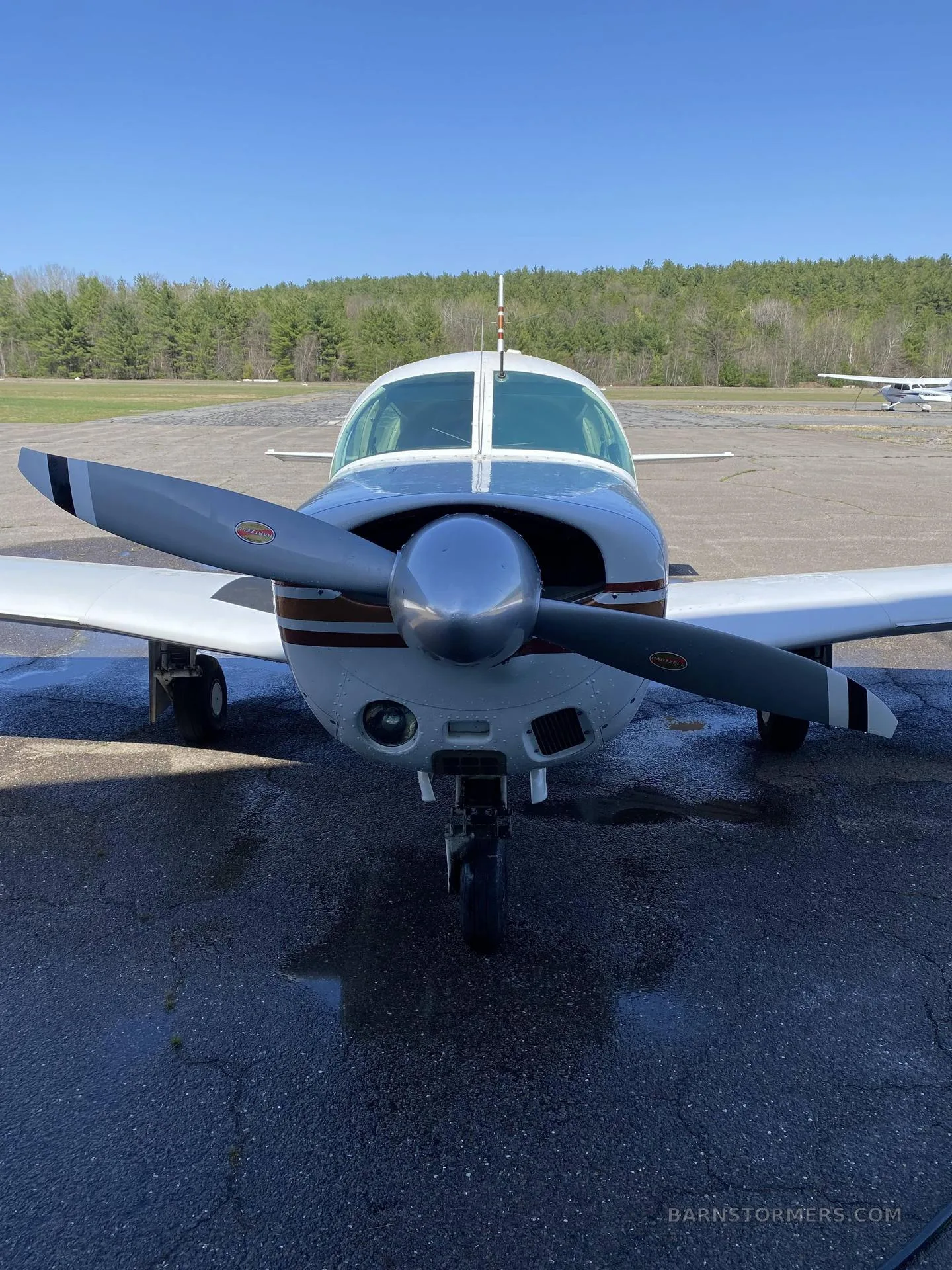 Front view of a white and brown single-engine propeller aircraft on an asphalt tarmac.