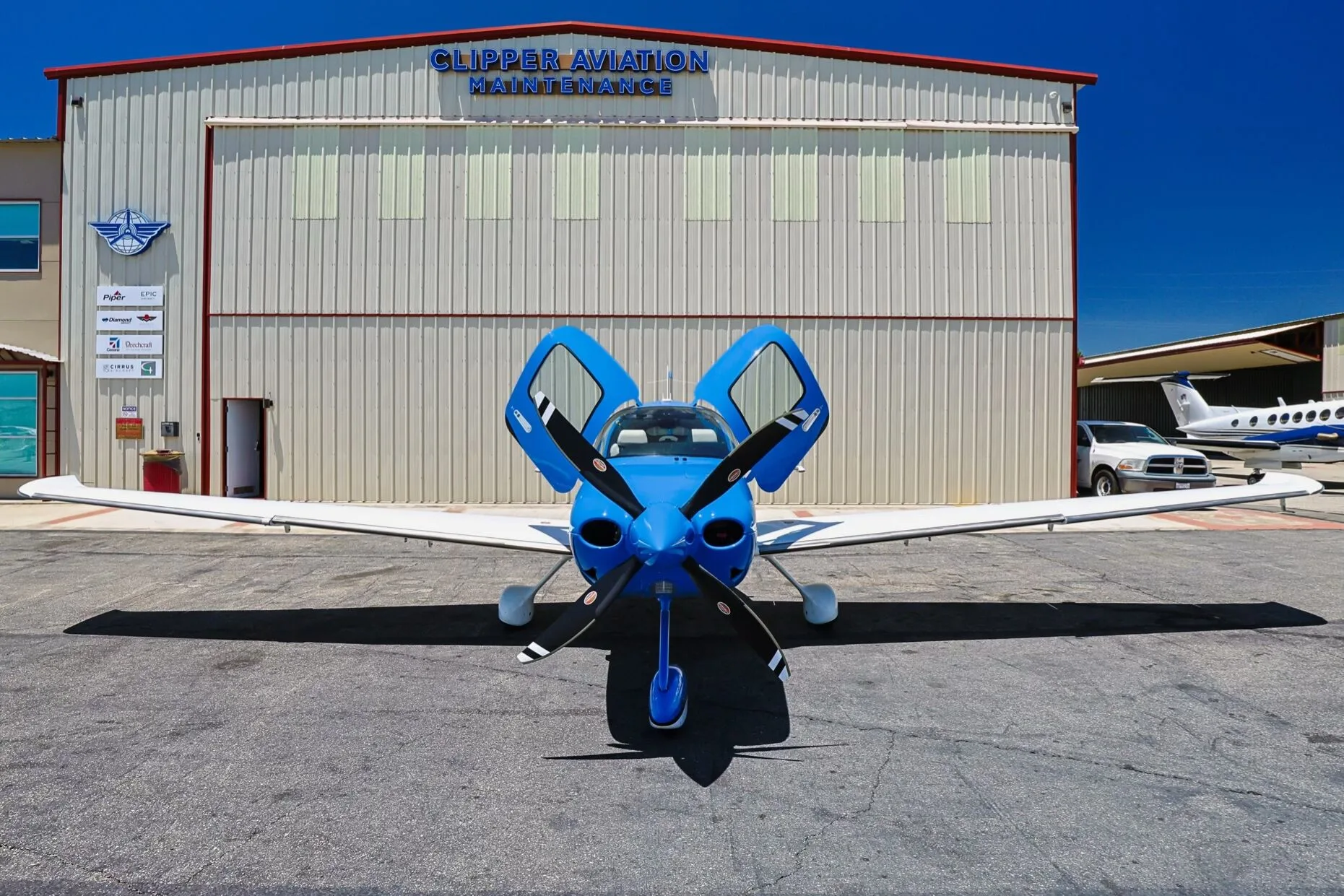 Front view of a blue and white Cirrus SR22 aircraft (N99W) with open doors, parked in front of a hangar.