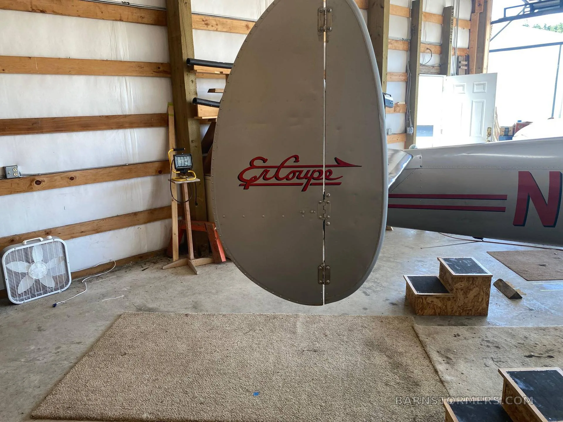 A close-up view of the silver Ercoupe aircraft's twin tail, featuring the red "Ercoupe" logo, inside a hangar.